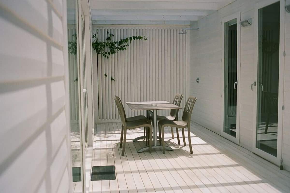 Een overdekt terras met een tafel en stoelen, een schuifpui en een witte buitenmuur.