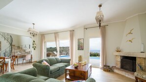 Un salon spacieux avec des canapés verts, une table basse en bois, une cheminée et une vue sur la mer.