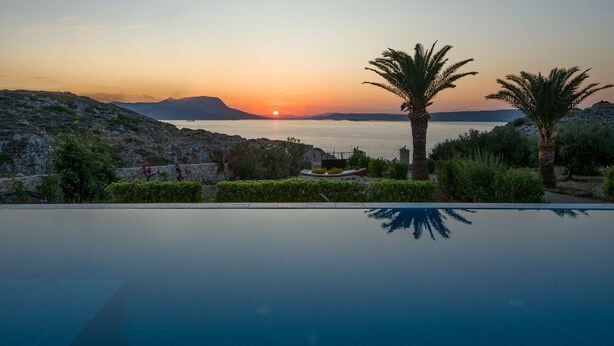 Une piscine offrant une vue sur le coucher de soleil, entourée de verdure et d’un paysage rocheux.