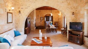 A cozy living room with a stone archway, a white sofa, a wooden coffee table, a TV, and a dining area with a table and chairs. - Villa Patriko Lux villa with pool next to Balos (Kissamos)
