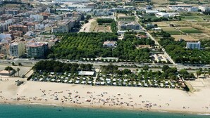 An aerial view of a coastal area with a beach, a parking lot, and buildings.