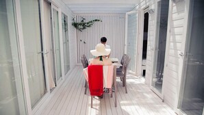 A covered outdoor area with a table and chairs, glass doors, and a white exterior wall.