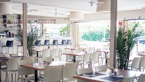 A spacious indoor dining area with white tables and chairs, large windows, and a bar area with shelves.
