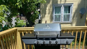 Una parrilla de barbacoa en una terraza de madera con una casa al fondo.