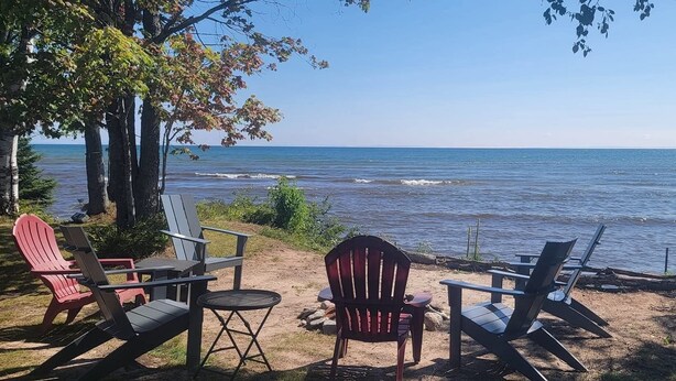 Un espacio de descanso frente a la playa con sillas tipo Adirondack y una mesita, con vistas al mar tranquilo.