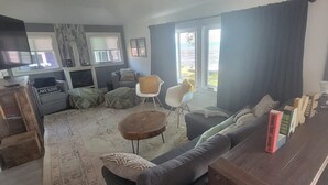 Una sala de estar con un sofá, sillas, una mesa de centro, un televisor y vistas al exterior.
