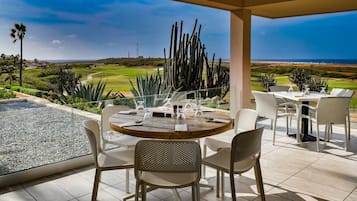 A patio with a round table and chairs, overlooking a golf course and ocean.