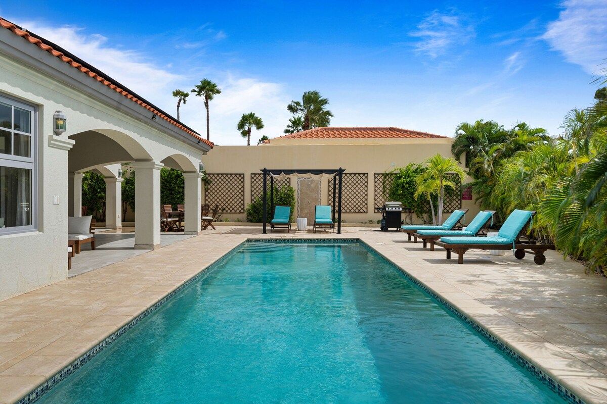 A swimming pool with lounge chairs and a covered seating area.