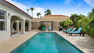 A swimming pool with lounge chairs and a covered seating area.