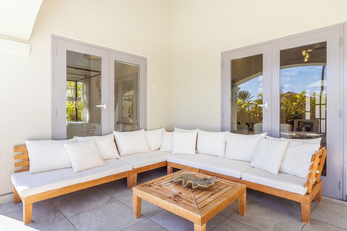 A modern outdoor seating area with a wooden bench and a sofa, large glass doors, and a view of the outdoors.