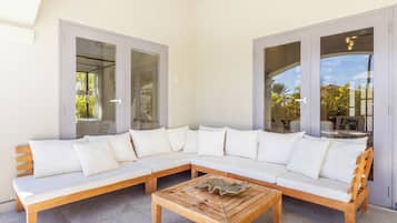 A modern outdoor seating area with a wooden bench and a sofa, large glass doors, and a view of the outdoors.
