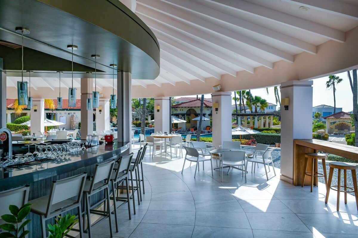 A modern outdoor bar area with a pool view, bar stools, and seating arrangements.
