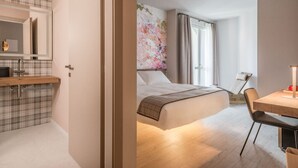 Ein modernes Hotelzimmer mit einem hölzernen Bett, einem Schreibtisch und einem Badezimmer mit Spiegel und Waschbecken.