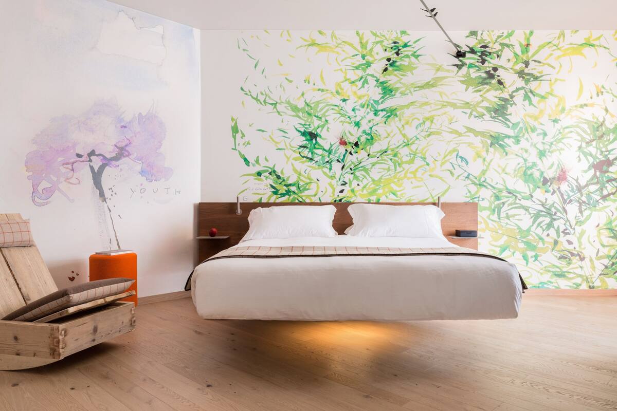 A modern bedroom with a large bed, a wooden headboard, and a wall mural.