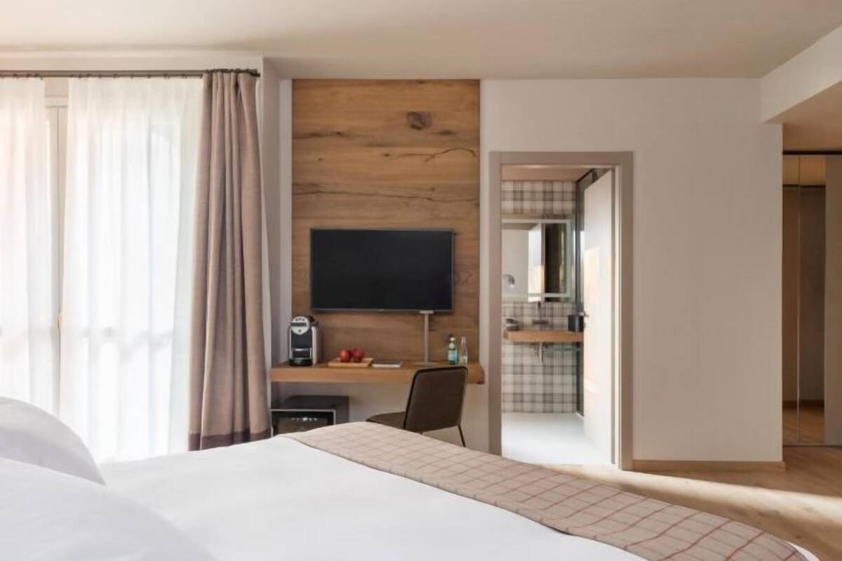 A hotel room with a bed, a desk with a computer, a TV, and a small kitchenette.