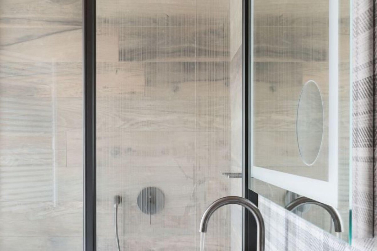 A shower with a glass door, a metal faucet, and a visible drain.