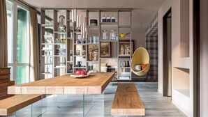 Ein modernes Esszimmer mit einem Holztisch und Bänken, einem Hängekorbstuhl und einem Bücherregal voller verschiedener Gegenstände.