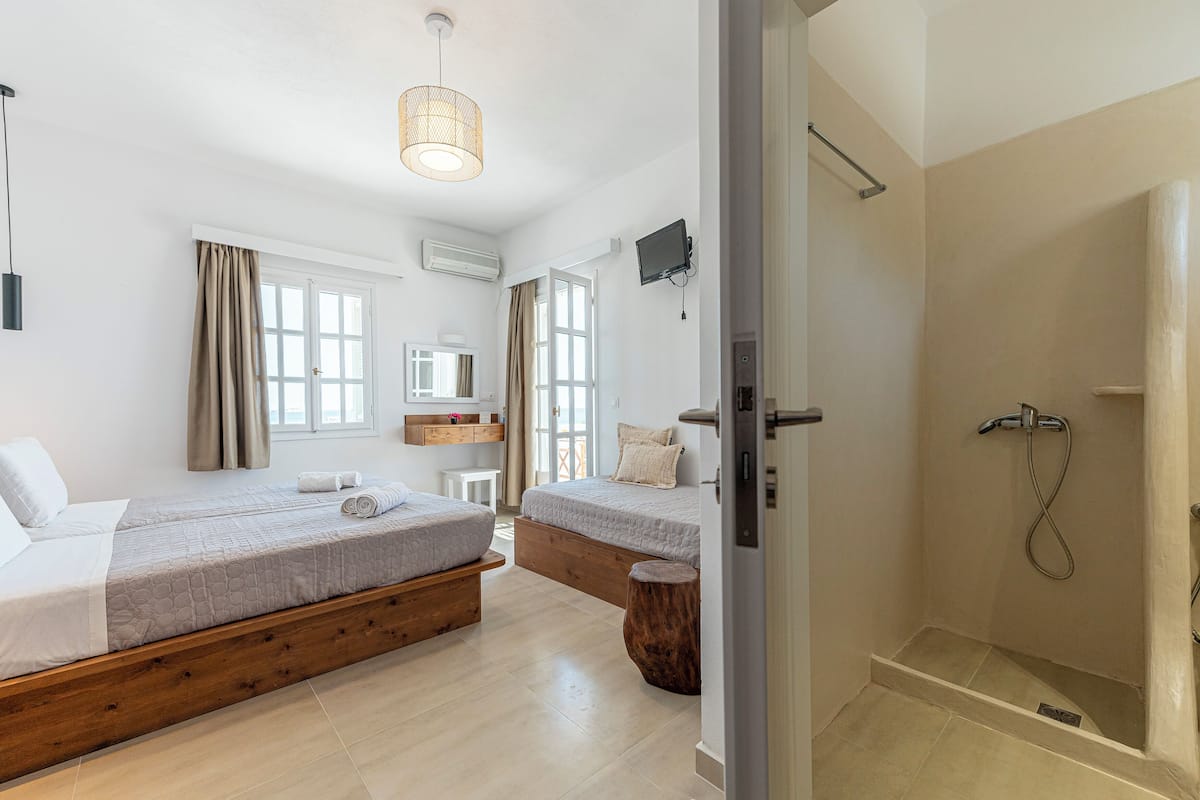 Un dormitorio moderno con dos camas, ducha y un ventanal grande.