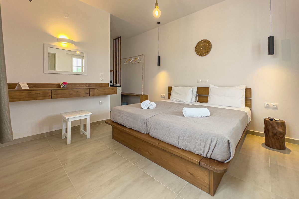Un dormitorio con una cama de madera, una mesita de noche, un banco, un espejo y una lámpara colgante.