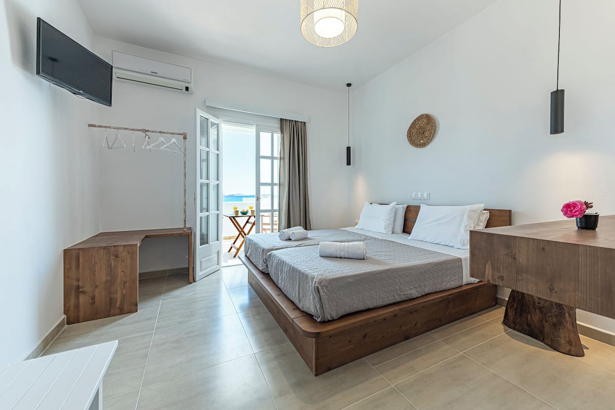 Un dormitorio moderno con una cama grande, cabecera de madera, mesitas de noche, un televisor y vista al mar a través de un ventanal amplio.