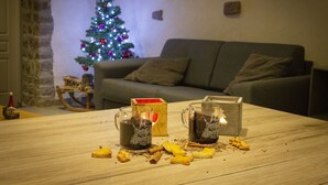 Un salon chaleureux avec une table en bois, deux tasses de chocolat chaud et un sapin de Noël en arrière-plan.