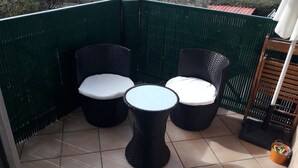 Angolo salotto con due poltrone in vimini e un tavolino rotondo, circondato da una recinzione verde.