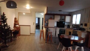 Una cucina moderna con mobili bianchi, un piano cottura nero e un forno a microonde. C'è una zona pranzo con un tavolo in legno e sedie nere. Si nota una piccola albero di Natale nell'angolo.