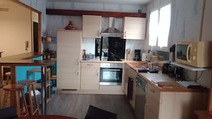 Una cucina compatta con piano cottura, forno, microonde ed elettrodomestici essenziali. Sono presenti sgabelli e un tavolo, che indicano una zona pranzo.