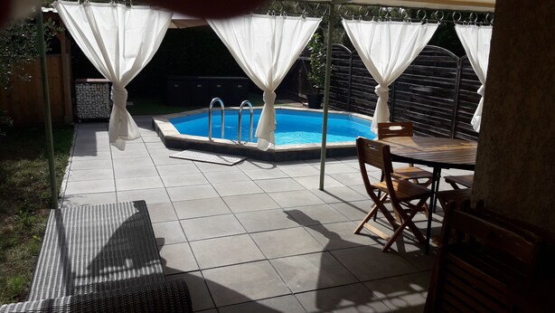 Un giardino sul retro con piscina, una zona patio coperta con tavolo e sedie, e un prato.