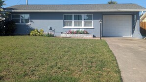 A two-story house with a garage, a small front yard with flowers, and a utility pole.