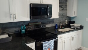 A kitchen with white cabinets, a black stove, a microwave, and a sink.