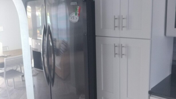 A kitchen with white cabinets, a black refrigerator, and a wooden floor.