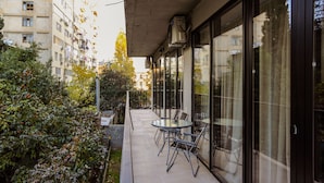 Un balcón con cerramiento de vidrio, mobiliario exterior y vista a un edificio residencial.