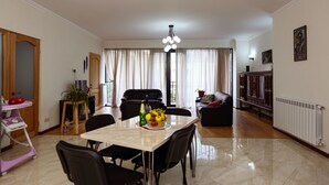 Un comedor con una mesa de mármol, sillas negras y un frutero. Se observa un sofá negro y un aparador al fondo.