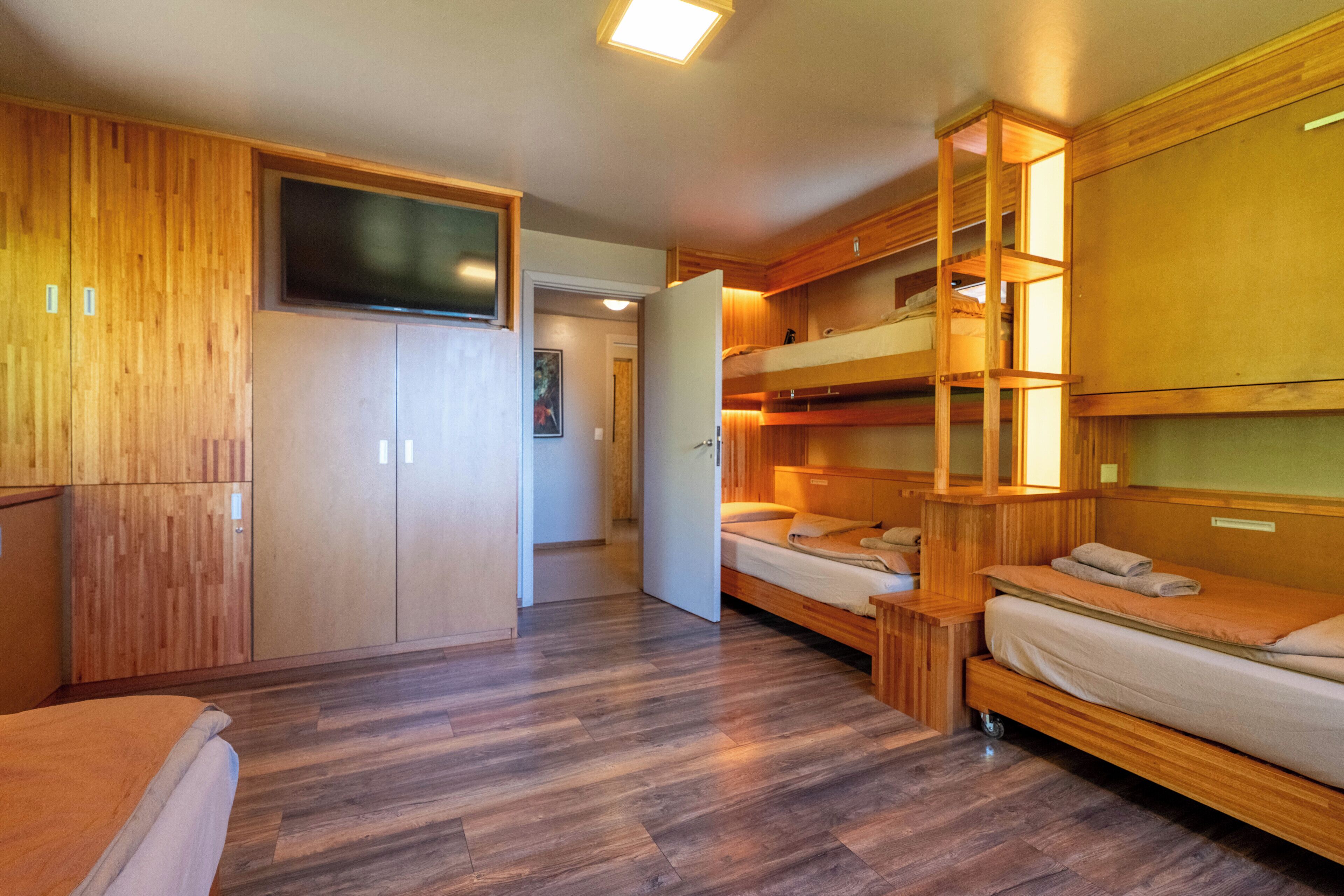 Una habitación con literas, televisión, armarios de madera y piso de madera.
