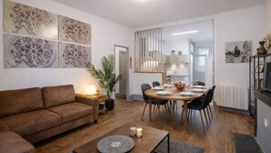 A modern living room with a brown sofa, a dining table set for four, and a kitchen in the background.