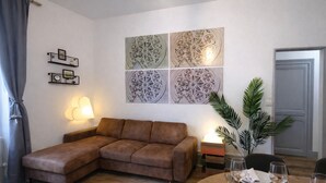 A living room with a brown sofa, a dining table set with plates and glasses, and a wall with decorative panels.