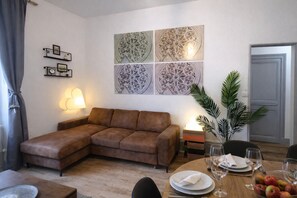 Uma sala de estar com um sofá marrom, uma mesa de jantar posta com pratos e copos, e uma parede com painéis decorativos.