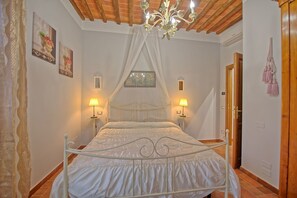 A bedroom with a canopy bed, two bedside lamps, a chandelier, and a door with a hanging bag.