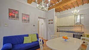 Un salon avec un canapé bleu, une table à manger avec des chaises et un coin cuisine équipé de placards et d’une cuisinière.