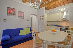 Un salon avec un canapé bleu, une table à manger avec des chaises et un coin cuisine  équipé de placards et d’une cuisinière.
