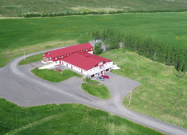 A large building with a red roof, surrounded by green fields and a winding road.