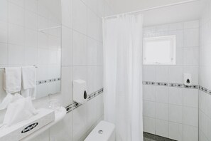 A bathroom with white tiles, a toilet, a sink with a soap dispenser, and a shower curtain.