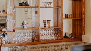 Una zona de bar con barra de madera, estantes que muestran vasos, botellas y objetos decorativos.