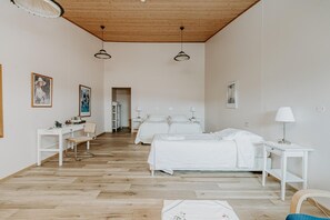A hotel room with a wooden ceiling, white walls, a bed, a desk, and a chair.