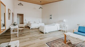 Habitación de hotel con techo de madera, paredes blancas, una cama grande, un escritorio, una silla, un sofá azul y una alfombra estampada.