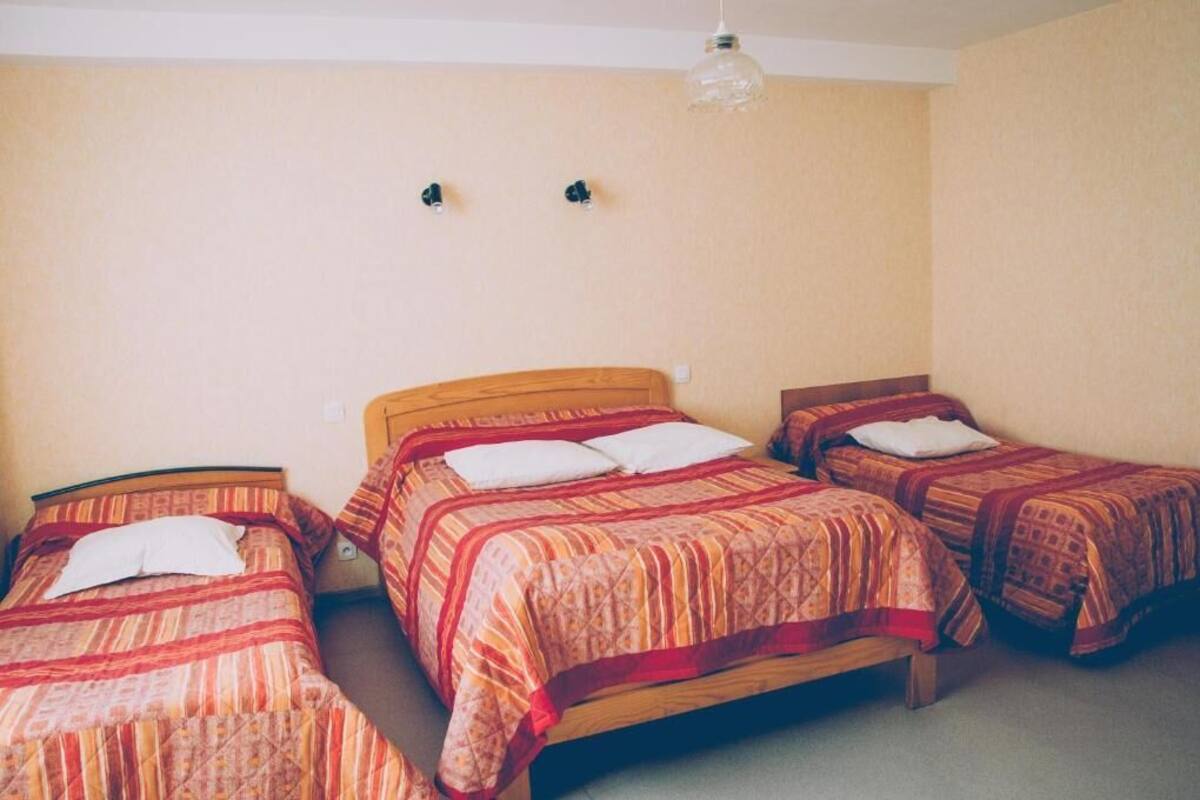 A room with three single beds, each with a patterned bedspread and pillows. There is a hanging light fixture above the beds.