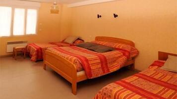Een slaapkamer met drie eenpersoonsbedden, een houten hoofdbord, een klein tafeltje en een raam met jaloezieën.