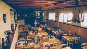 A restaurant with wooden tables and chairs, a bar area, and a view of the street. - Hotel Restaurant Maurice (Chateauroux)