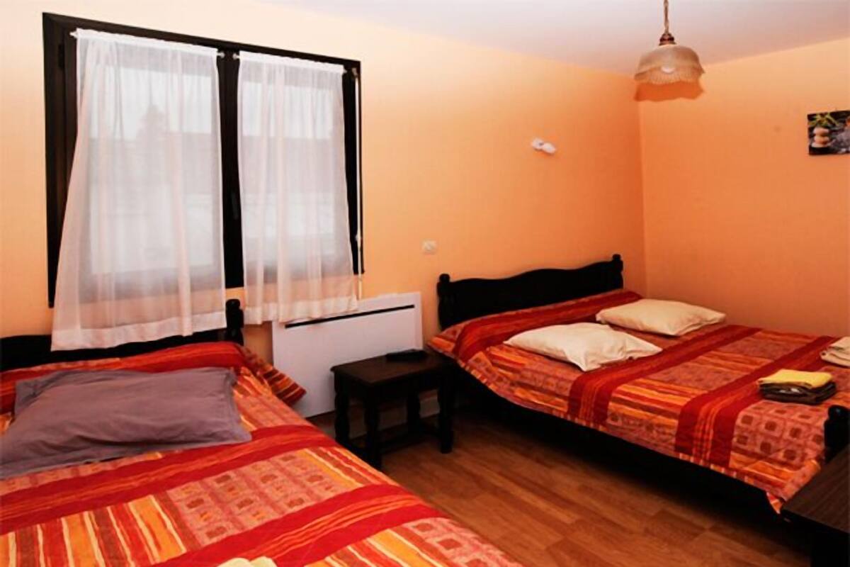 A room with two beds, a small table, a heater, and a hanging light fixture.